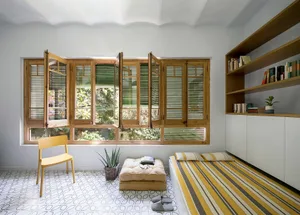 A minimalist bedroom with a large window, wooden furniture, and a striped rug.