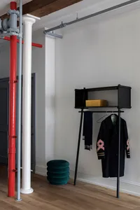 A minimalist space featuring a metal clothing hanger with a scarf and coat hanging on it, set against a white wall.