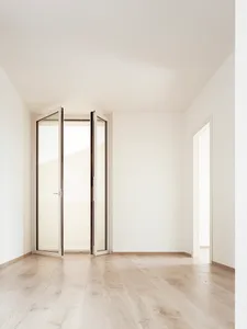 An empty room with minimalist design, featuring wood paneling and an open door leading to another room.