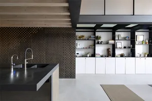 Modern minimalist kitchen with concrete countertops, perforated metal backsplash, and white wood cabinets.