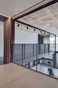 Minimalist office interior featuring a metal mesh partition on a concrete ceiling and wooden floor.