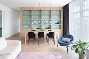 A minimalistic residential interior featuring wooden furniture, glass pendant lights, and soft textiles.