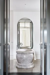 A modern bathroom with a marble bathtub and a tall, oval-shaped mirror on the wall.