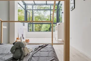 A minimalistic bedroom with a wooden frame bed, looking out to a green outdoor space through large windows.
