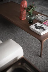 A sleek, modern coffee table crafted from wood, adorned with a red sculpture, green vase with red berries, and architectural 