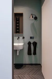 A modern concrete bathroom with a small sink, mirror, and towel hooks.