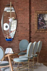 Modern dining room featuring glass table, metal chairs, and artwork on a brick wall.