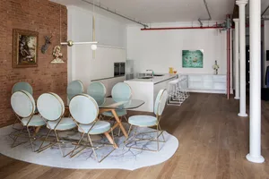 Modern residential space featuring a dining table with blue upholstered chairs and metal framing, a kitchen island, and a bri