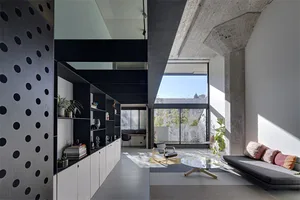 A spacious, modern living room with concrete walls and floor, featuring a sofa, coffee table, and bookshelf.