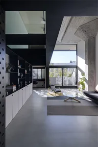 Modern living room with minimalist design featuring concrete flooring, glass coffee table, and industrial style furniture.