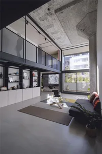 Modern living room with concrete flooring, glass coffee table, and minimalist decor.