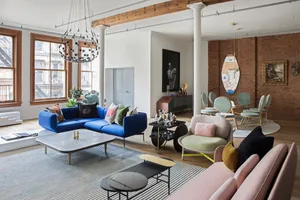 A modern living room featuring colorful furniture, exposed wooden beams, and a large blue sofa.