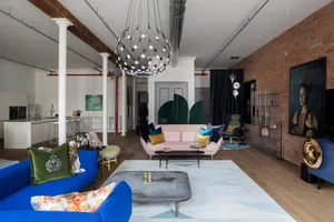 A modern living room with pastel-colored sofas and a geometric rug, featuring industrial-style lighting and exposed brick wal