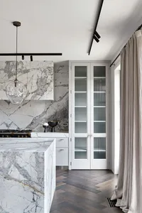 A modern kitchen with marble countertops and flooring, featuring white cabinetry and a minimalist design.