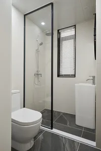 Modern minimalist bathroom with a glass shower enclosure, a white toilet, and a pedestal sink, all set against a grey and whi