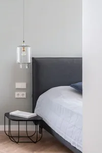 Modern minimalist bedroom with a fabric bed, glass pendant light, and wooden floor.