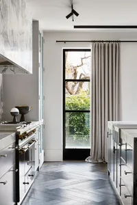 Modern residential kitchen with marble countertops and herringbone wooden flooring.