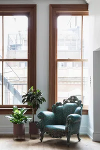 A modern, blue, scale-shaped armchair in a living space with a large window and plants.