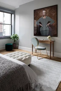 A stylish bedroom interior with a white tufted pouf, grey rug, and high-end furniture.
