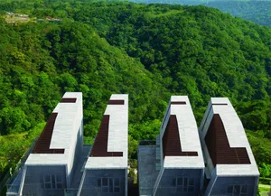 A cluster of four modern cement buildings surrounded by lush greenery on a hillside.