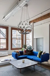 Modern living room featuring a blue sofa, industrial chandelier, and large windows.