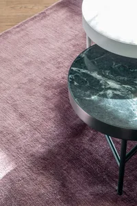 A modern marble side table with a metallic base on a plush pink rug.