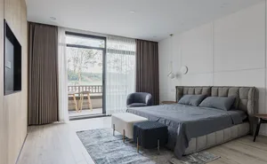 A modern minimalist bedroom with grey bedding, a upholstered bed frame, and a flat-screen TV mounted on the wall.