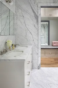 Modern bathroom featuring marble walls and flooring, white cabinets, and a double sink.