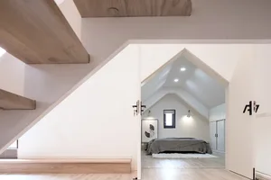 A modern minimalist bedroom with a wooden staircase and white walls.