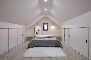 A modern minimalist bedroom featuring a bed with a gray blanket, a white fluffy rug, and a window with a white frame.