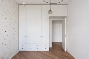 A modern bedroom featuring white cabinets, paper-patterned wallpaper, and hardwood floors.