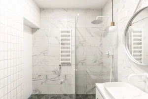 A modern bathroom with marble tiles and a glass shower enclosure.