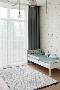 A minimalist bedroom with a wood frame bed, grey curtains, and a patterned rug.