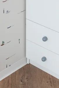 Modern white drawers with blue knobs on wooden floor with printed wallpaper background.