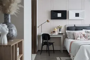 A cozy minimalist bedroom with a comfortable bed, decorative pillows, and a small desk with a lamp and vase.