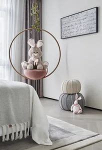 A minimalist child's bedroom with a white bed, gray curtains, and a hanging pink cushion for a rabbit plush toy.