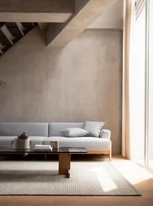 A minimalist living room featuring a concrete wall and floor, with a grey sofa and a black coffee table.
