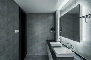 A modern bathroom with black and gray ceramic tiles, a white countertop sink, and a large rectangular mirror.