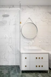 A modern bathroom featuring marble stone tiles and a white sink on a white vanity with gold handles.