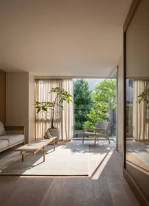 A modern living room featuring wooden furniture, light-colored curtains, and a potted plant by a window.