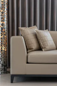 Modern sofa with plush gray leather cushions and geometric design, set against gray curtains.