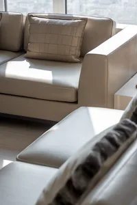 Modern, minimalistic living room with a white leather sofa adorned with a geometric-patterned pillow, illuminated by soft, na