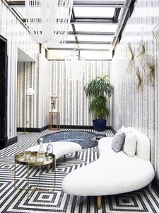 A modern living room with a white curvilinear sofa, a round metal table, a decorative floor lamp, and a large potted plant.