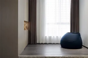 Modern minimalist living room with a navy bean bag chair, large windows with curtains, and a wooden floor.
