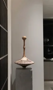 A modern sculpture made of wood with a patchwork design displayed on a pedestal.