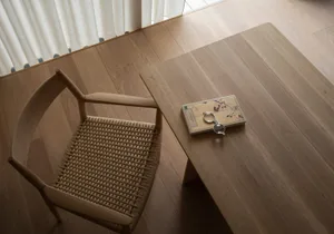 A wooden home office table with a woven basket seat on a wooden floor next to a curtain.