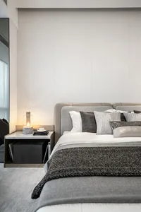 A modern bedroom with grey fabrics, including a bed with a grey headboard and multiple pillows, a marble nightstand with a la