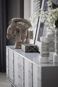 A modern decorative wooden horse sculpture placed on a sleek, white cabinet.