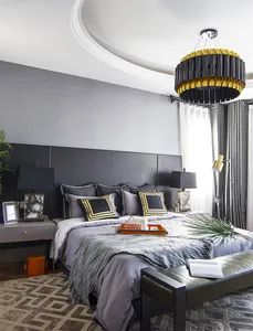 A modern grey bedroom featuring a black upholstered headboard, grey bedding, and a contemporary chandelier.