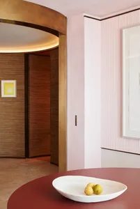 A modern interior design scene featuring a white table with a bowl of fruit, set against a pink textured wall and a wooden do